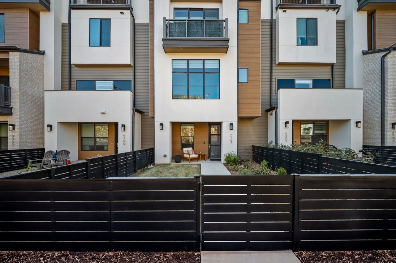 Front elevation of the modern townhome row at 4507 Unity Circle in The Grove, Austin, showing the wood and stucco facades and black perimeter fencing, built by M Signature.