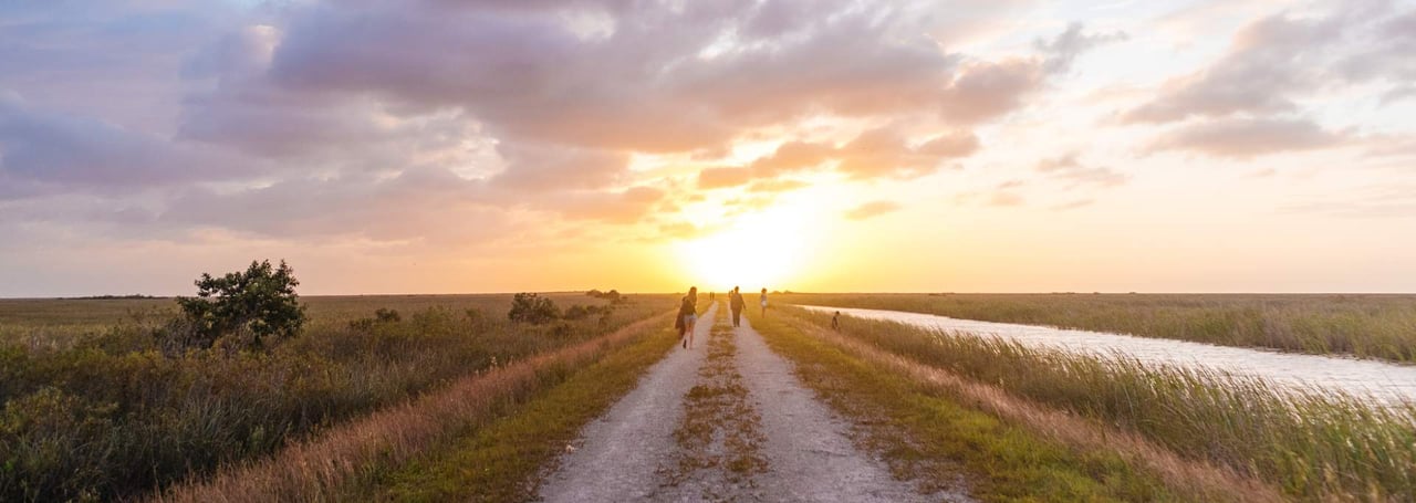 Sunset view of the Sawgrass Trailhead in Coral Springs, Florida with people walking along a gravel path.