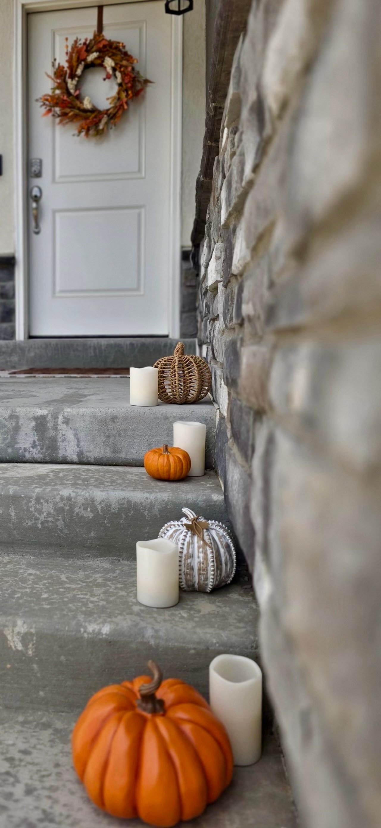 Stone front steps with pumpkins and candles lead to a white door with an autumn wreath.