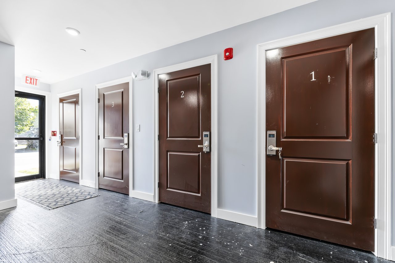 Residential hallway with numbered brown doors and a glass exit door.
