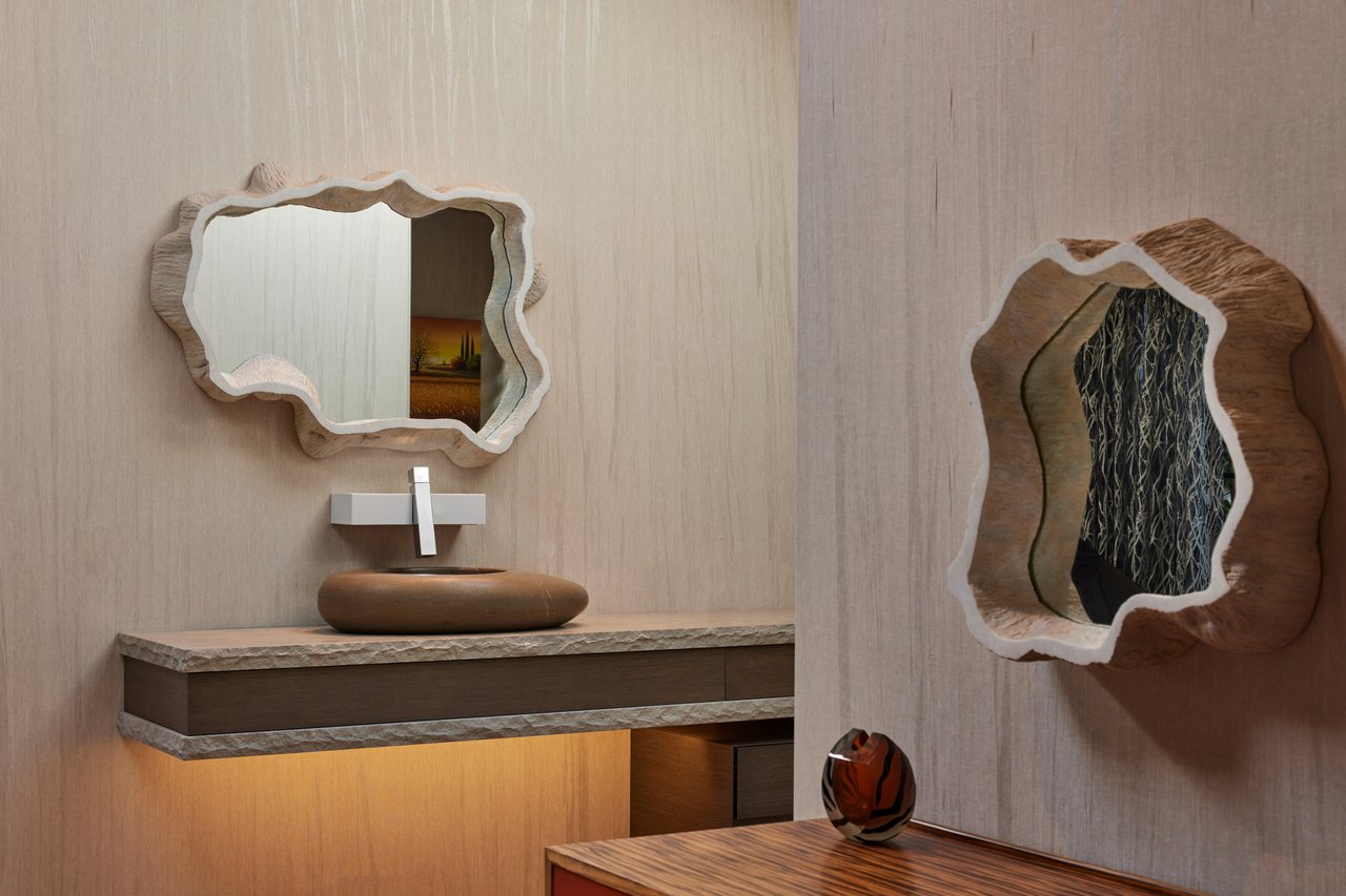 Modern bathroom with a floating wood vanity, sculptural vessel sink, and two irregular mirrors.