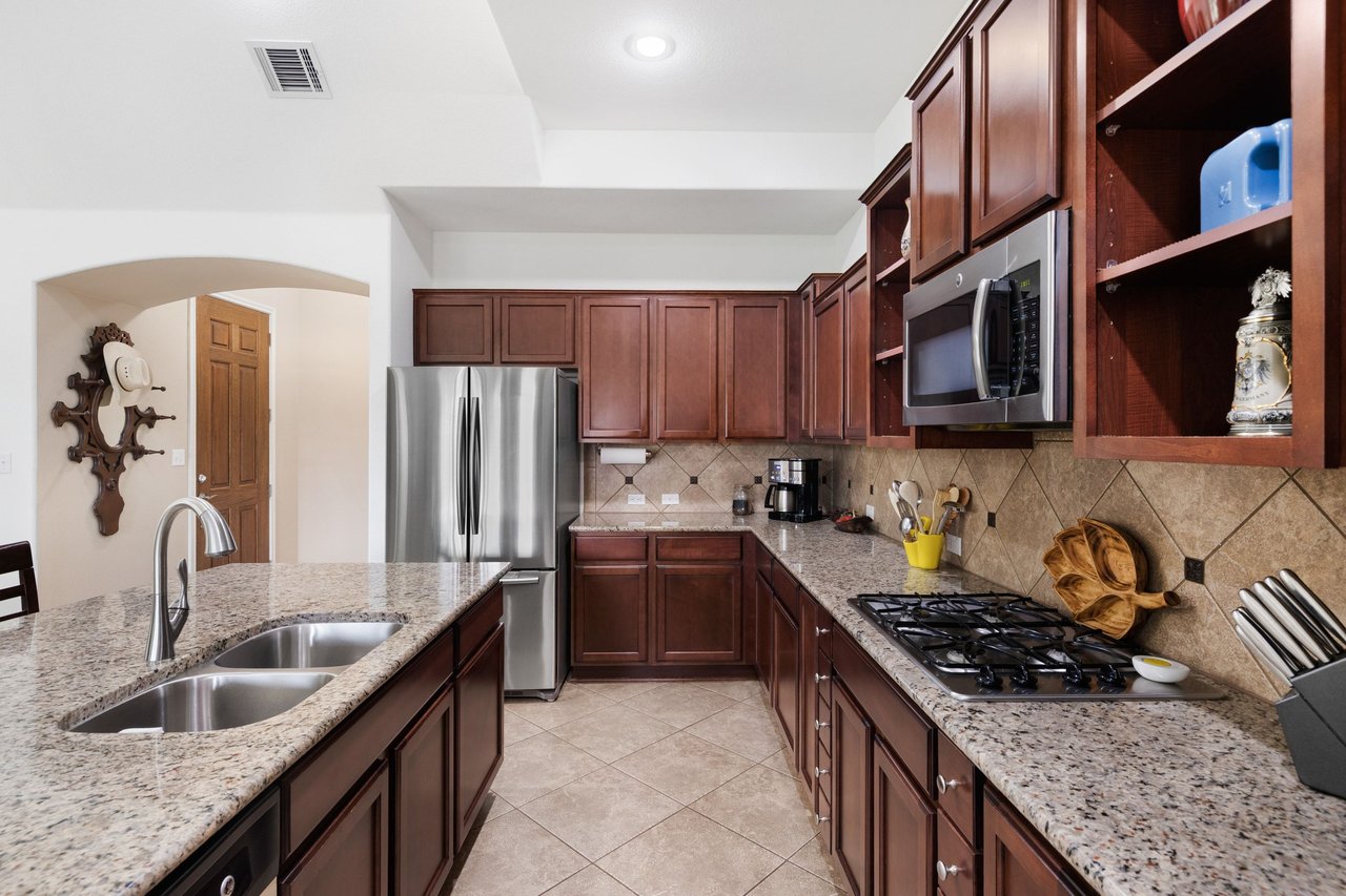 Kitchen with dark wood cabinets, granite counters, a double sink, stainless appliances, and a gas cooktop.