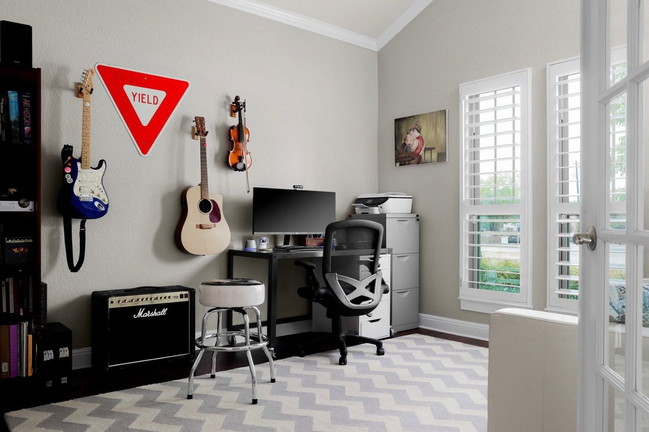 Home office with wall-mounted guitars, a computer desk, Marshall amplifier, and tall shuttered windows.