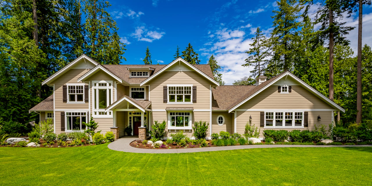 Beige, gabled house with a curved walkway, landscaped beds, and a broad green lawn.