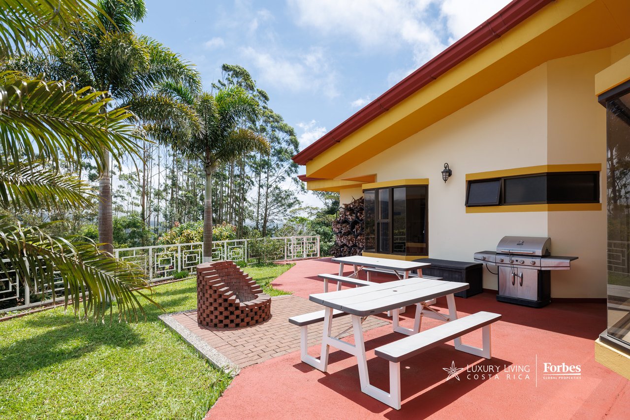 House patio with white picnic tables, a barbecue grill, and palm trees along the lawn.