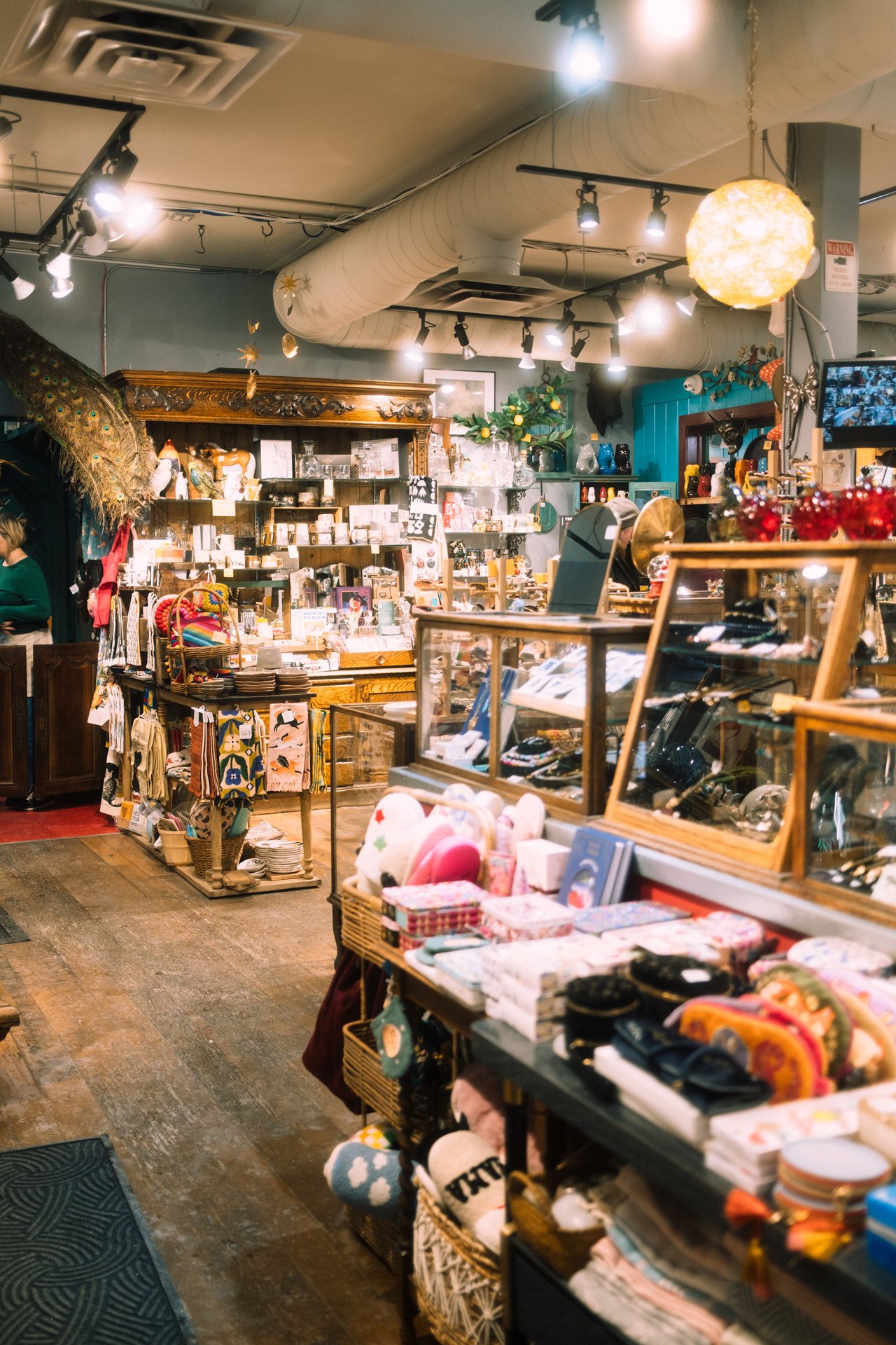 Gift shop interior filled with colorful homewares, textiles, and ceramics beneath a glowing globe pendant.
