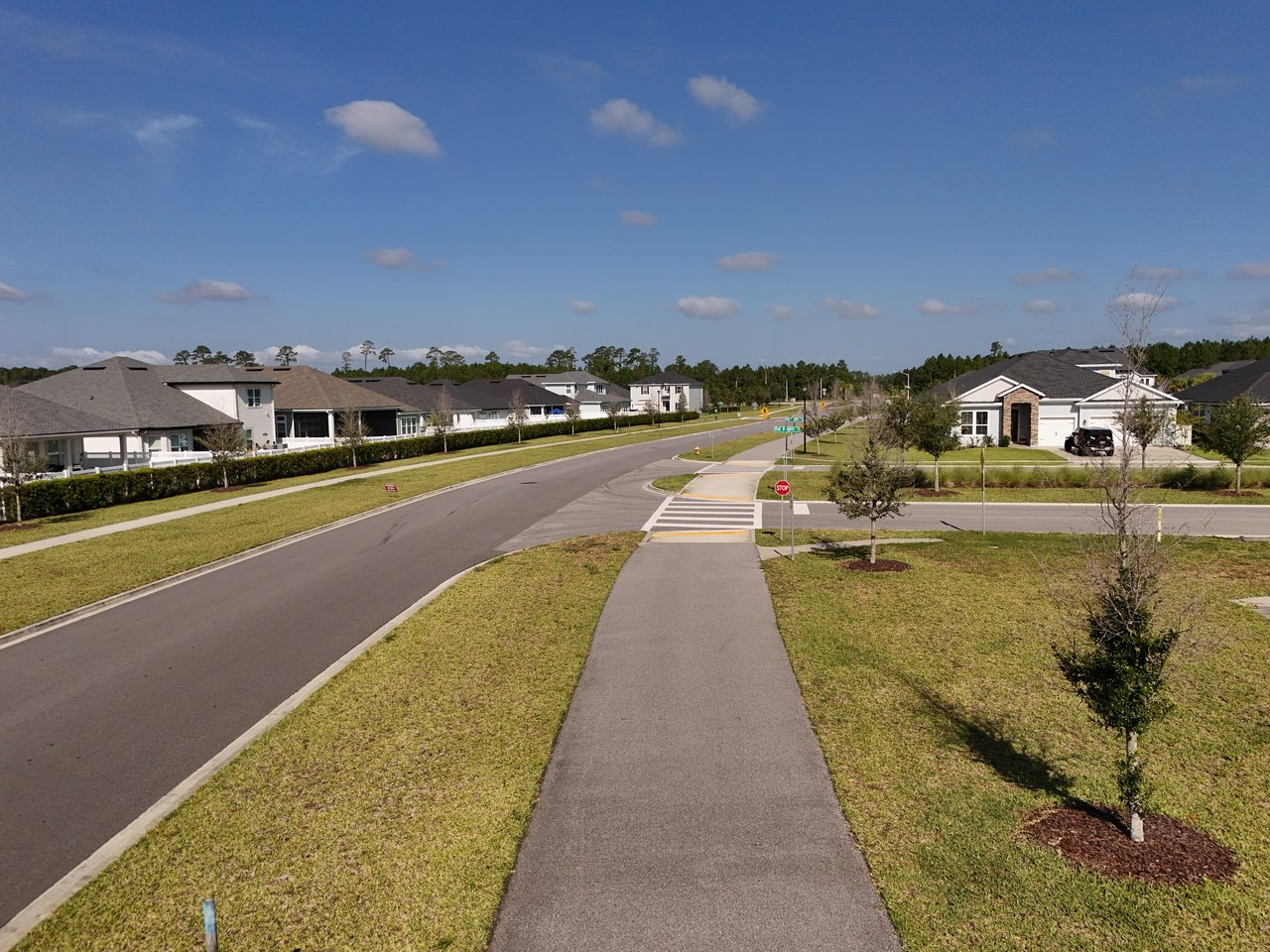 Residential street with single-story homes, landscaped lawns, sidewalks, and a crosswalk at an intersection.