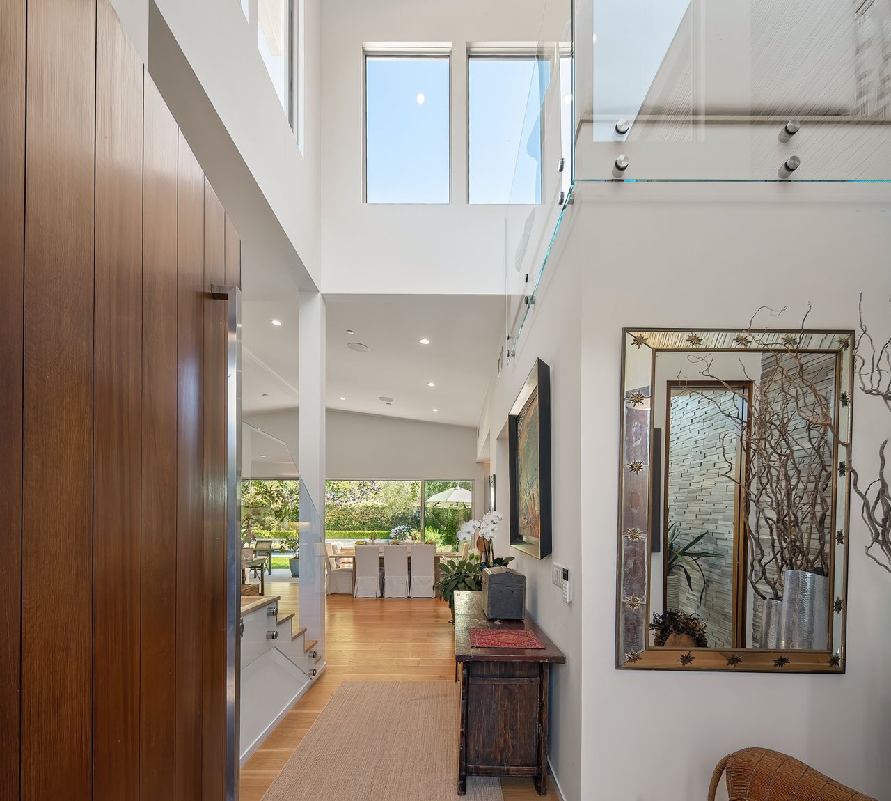 Double-height entry hall with wood-paneled doors, a glass railing, and views toward the dining area and garden.