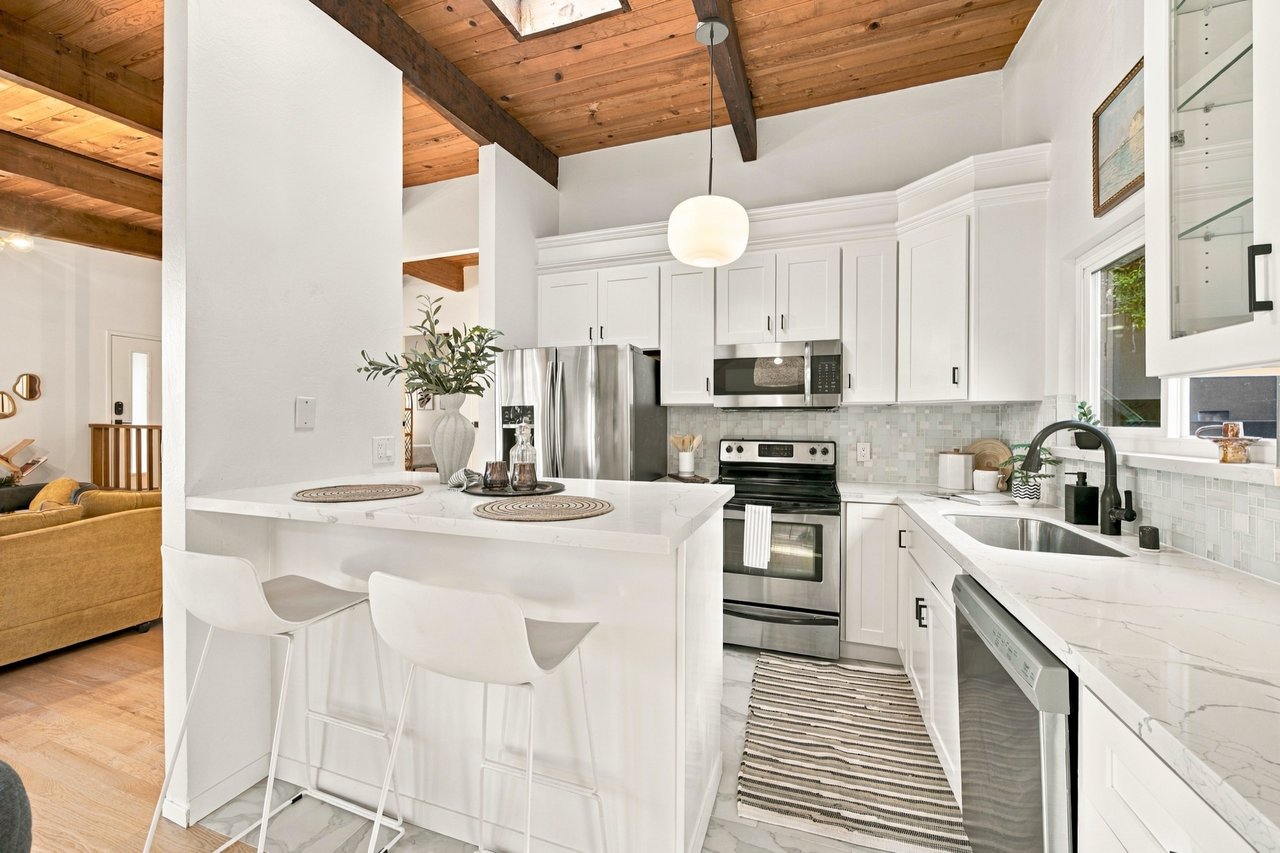 Bright kitchen with white cabinets, marble island, stainless appliances, and exposed wood ceiling beams.