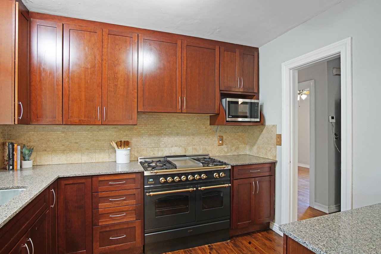 Warm kitchen with dark wood cabinets, granite countertops, and a black stove. A microwave is above the stove, and a utensil holder is on the counter.