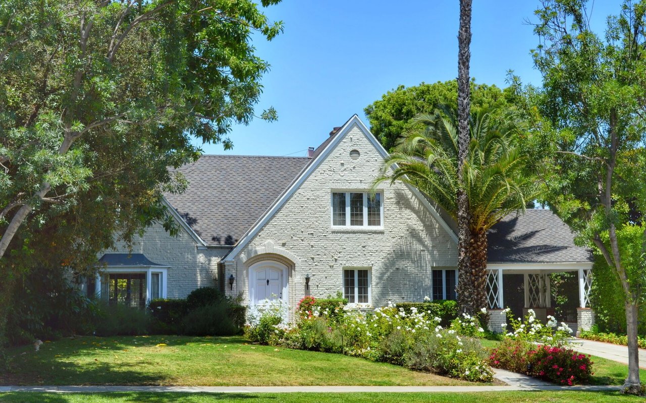 Light brick house with steep gables, an arched entry, and a flower-filled front garden.