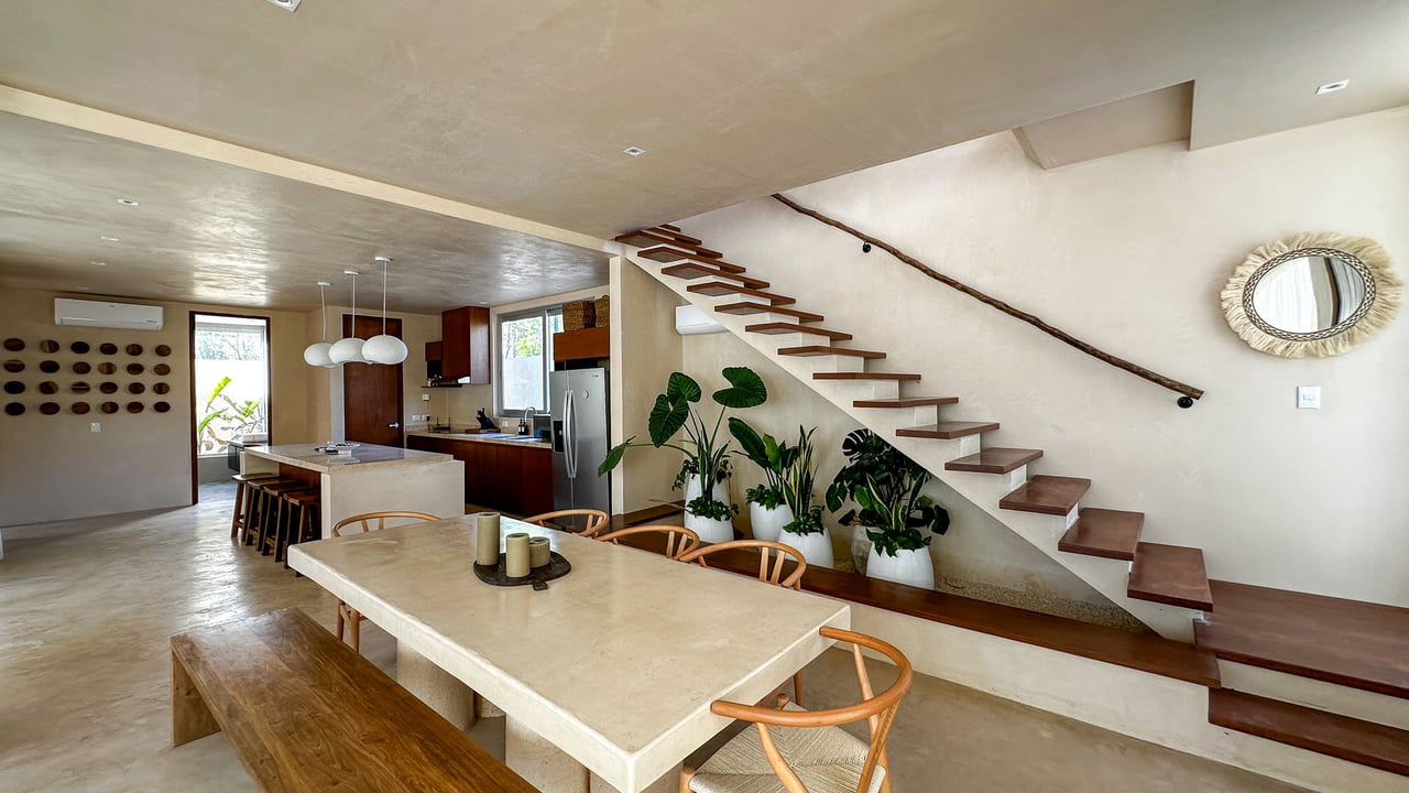 Open-plan kitchen and dining area with a stone island, potted plants, and floating wood staircase.