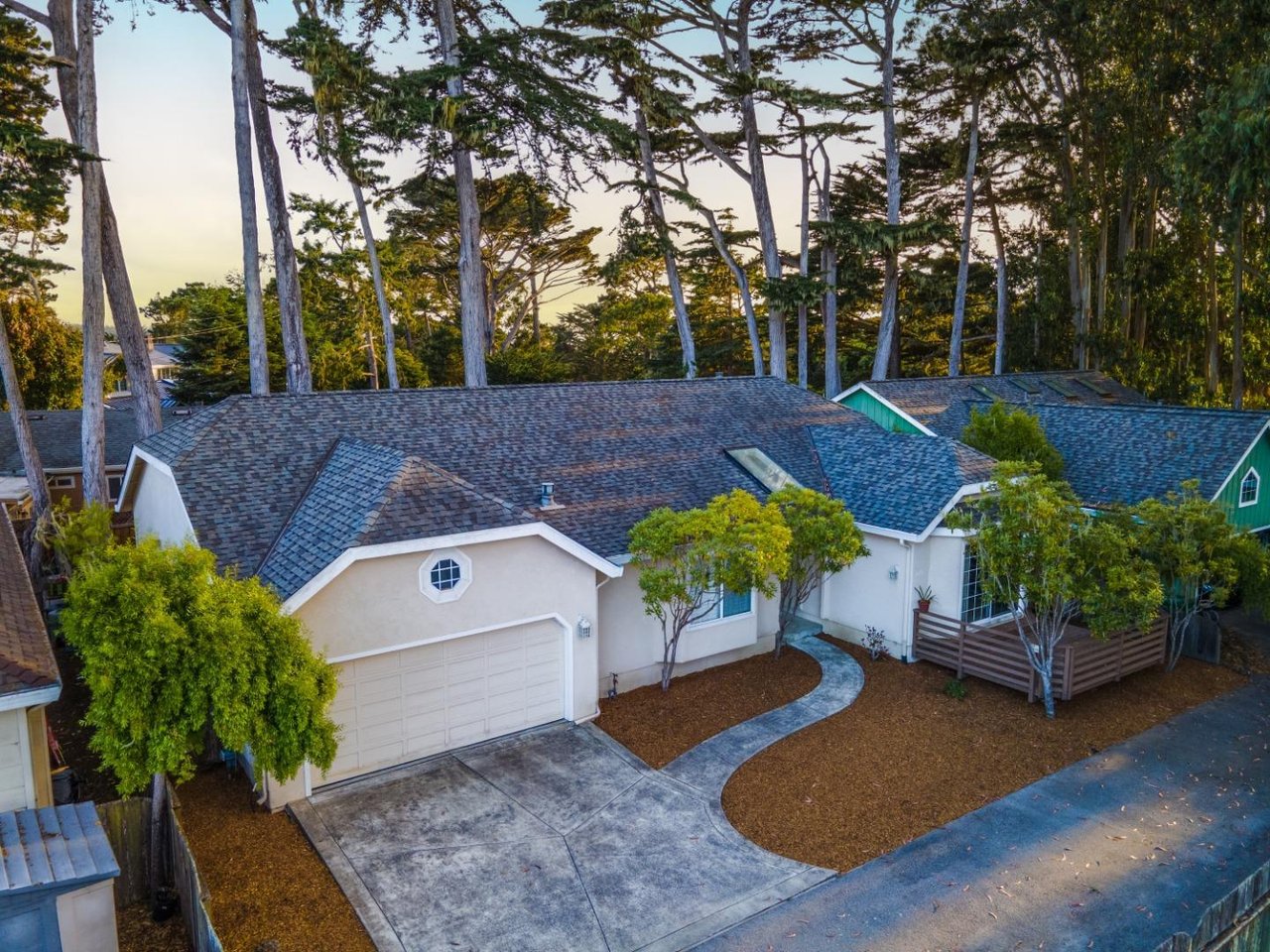 Aerial view of a single-story home with a garage and curved walkway beneath tall trees.