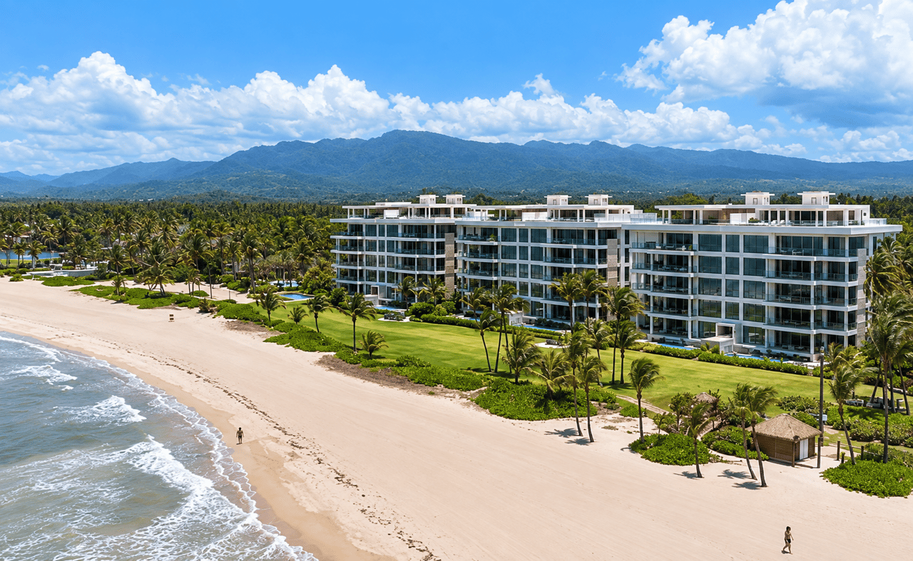 Modern beachfront residences beside a palm-lined beach, with ocean surf and mountains beyond.