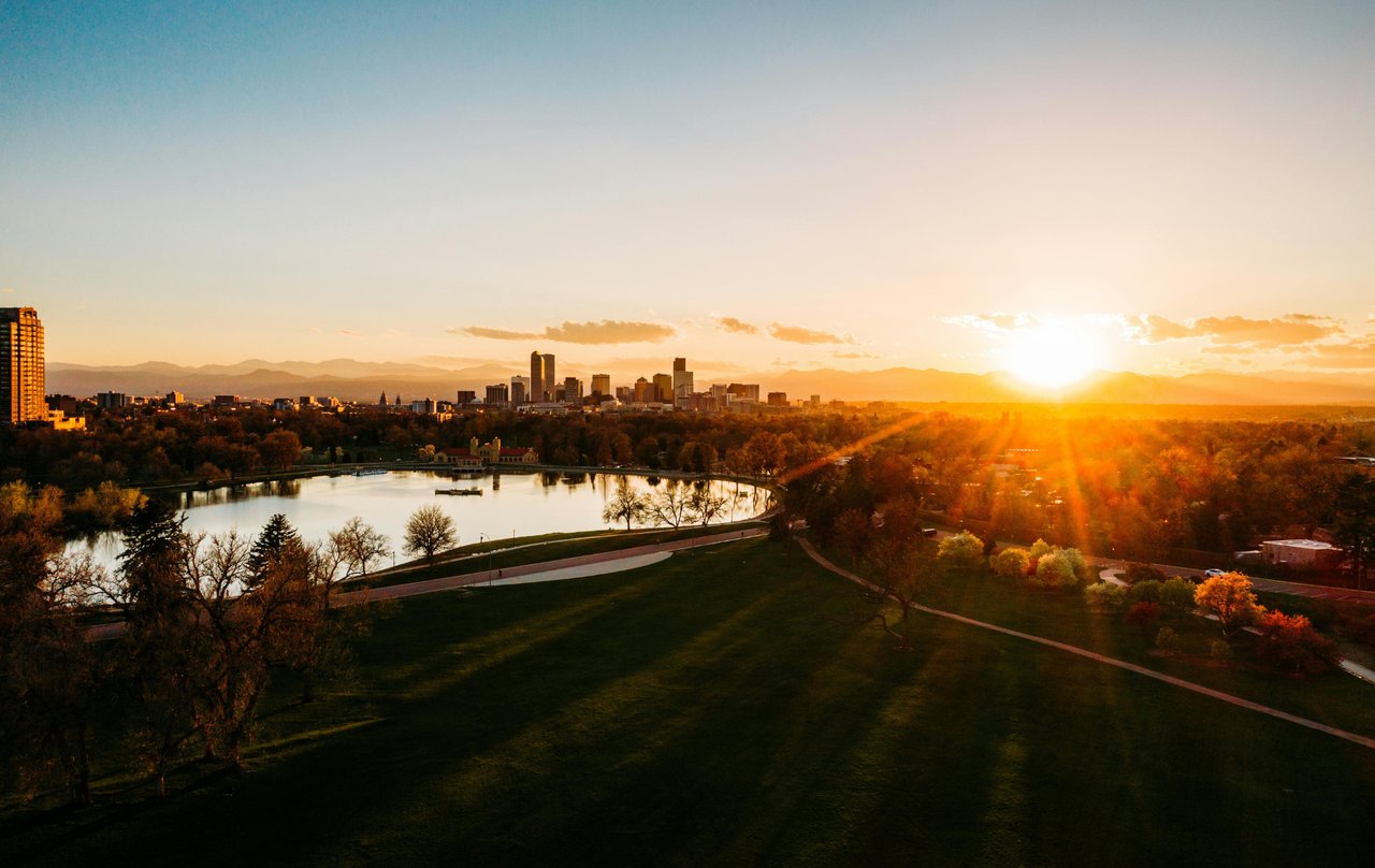Sunset over City Park with warm light reflecting on the water and Denver skyline