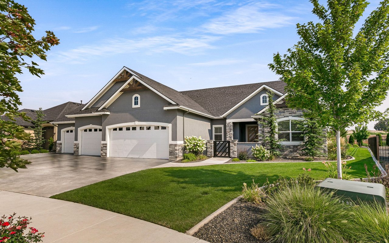 Gray home with stone accents, three-car garage, broad driveway, and landscaped front lawn.