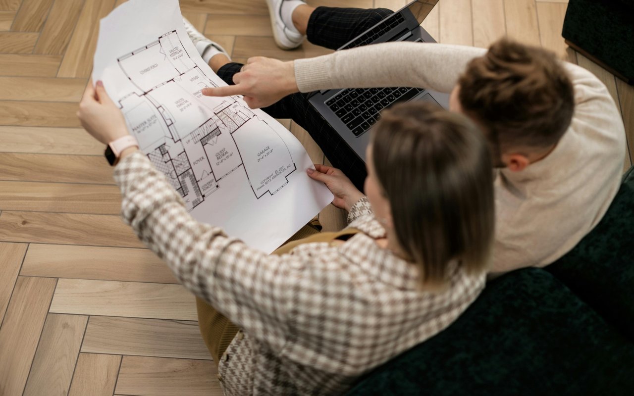 Two people review a home floor plan beside an open laptop.