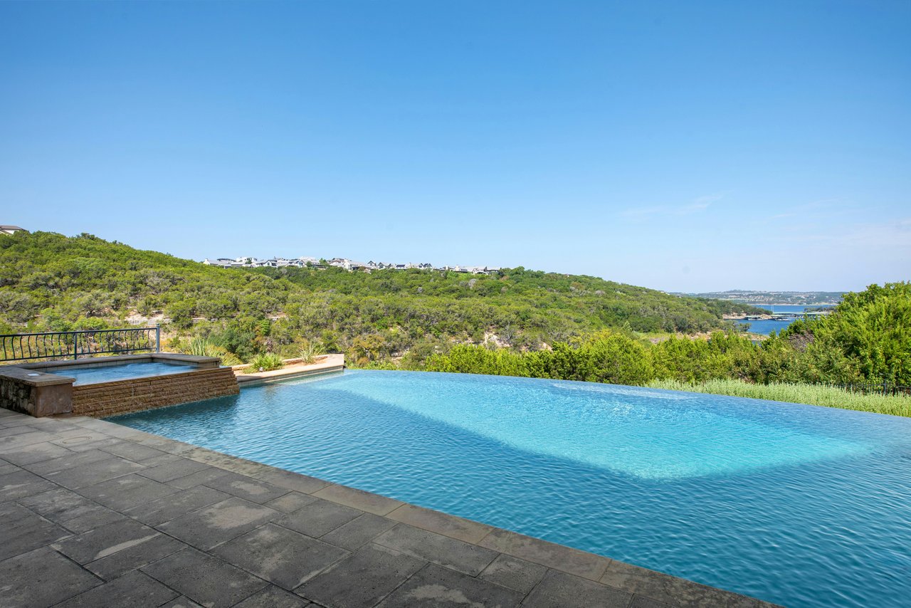 Infinity pool and raised spa overlook green hills and distant water.