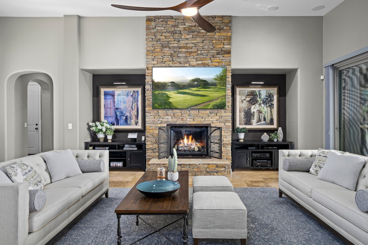 Staged living room with two sofas facing a coffee table and stone fireplace with TV above.