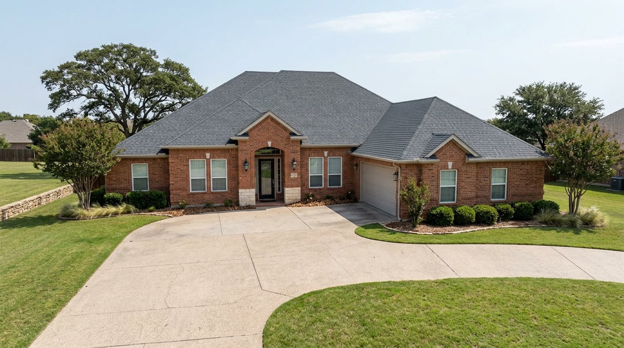 Red-orange brick estate with dark shingle roofs, a curving driveway, broad lawn, and mature live oaks.