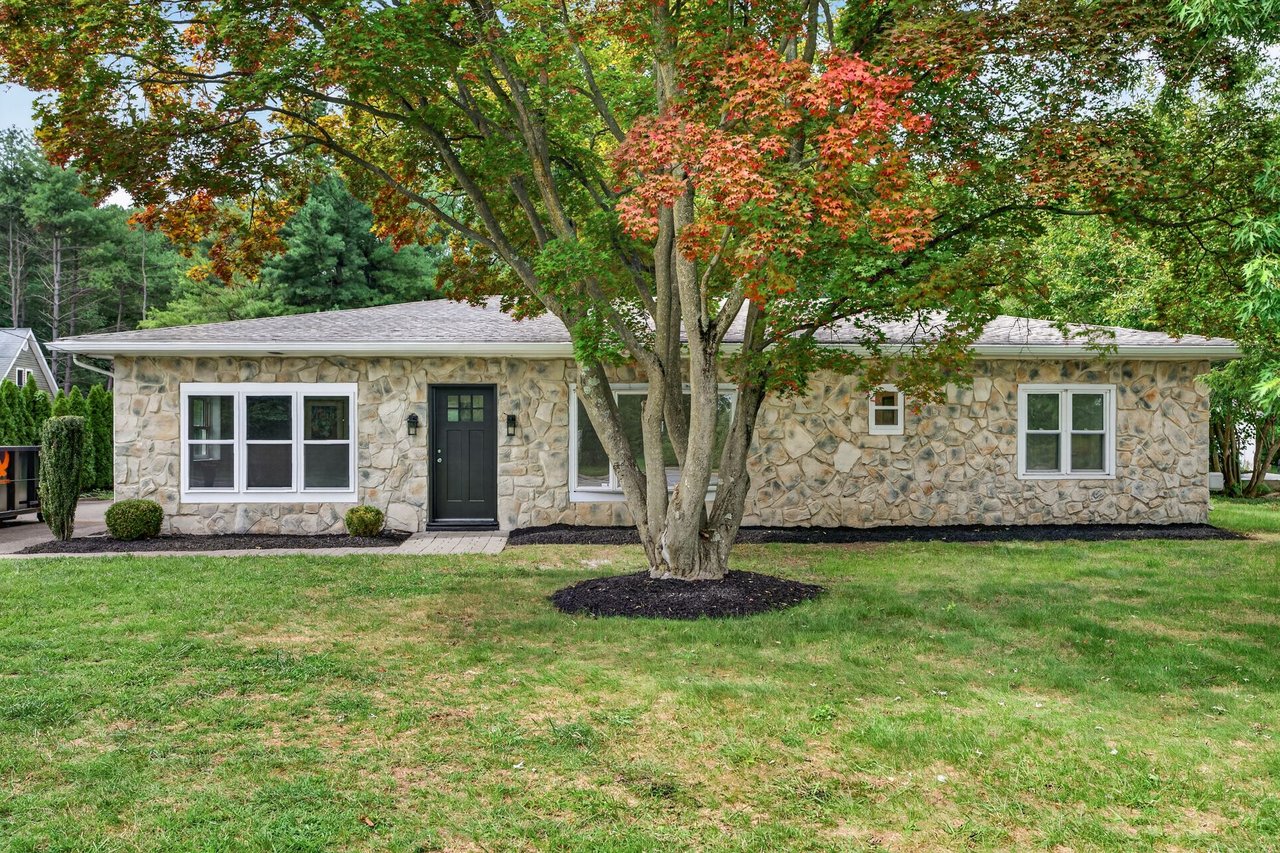 Stone ranch house behind a large tree with autumn foliage and a broad front lawn.