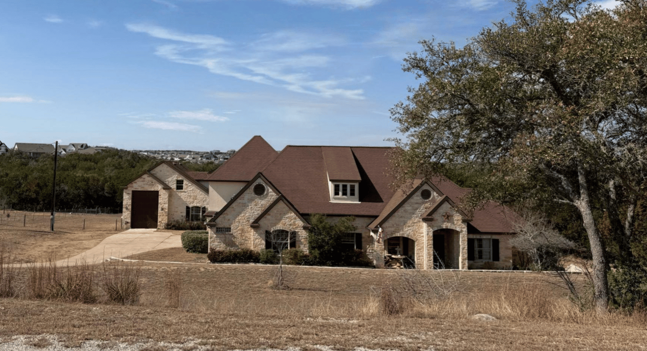 Large stone house with multiple gables, a wide driveway, and a dry grassy yard.