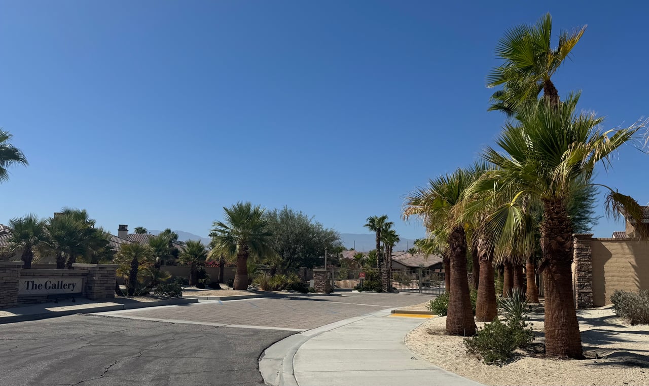 The Gallery community entrance with palm trees, desert landscaping, and distant mountains.