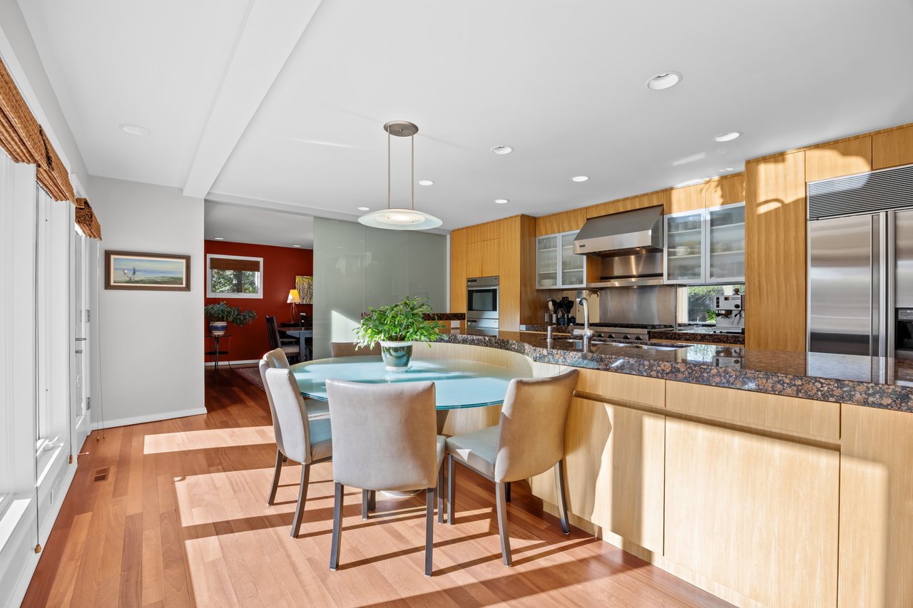 Kitchen and dining area with wood cabinetry, stainless steel appliances, and a round glass table.