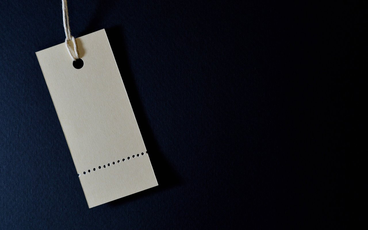 Blank cream price tag with a string and perforated edge on a dark navy background.