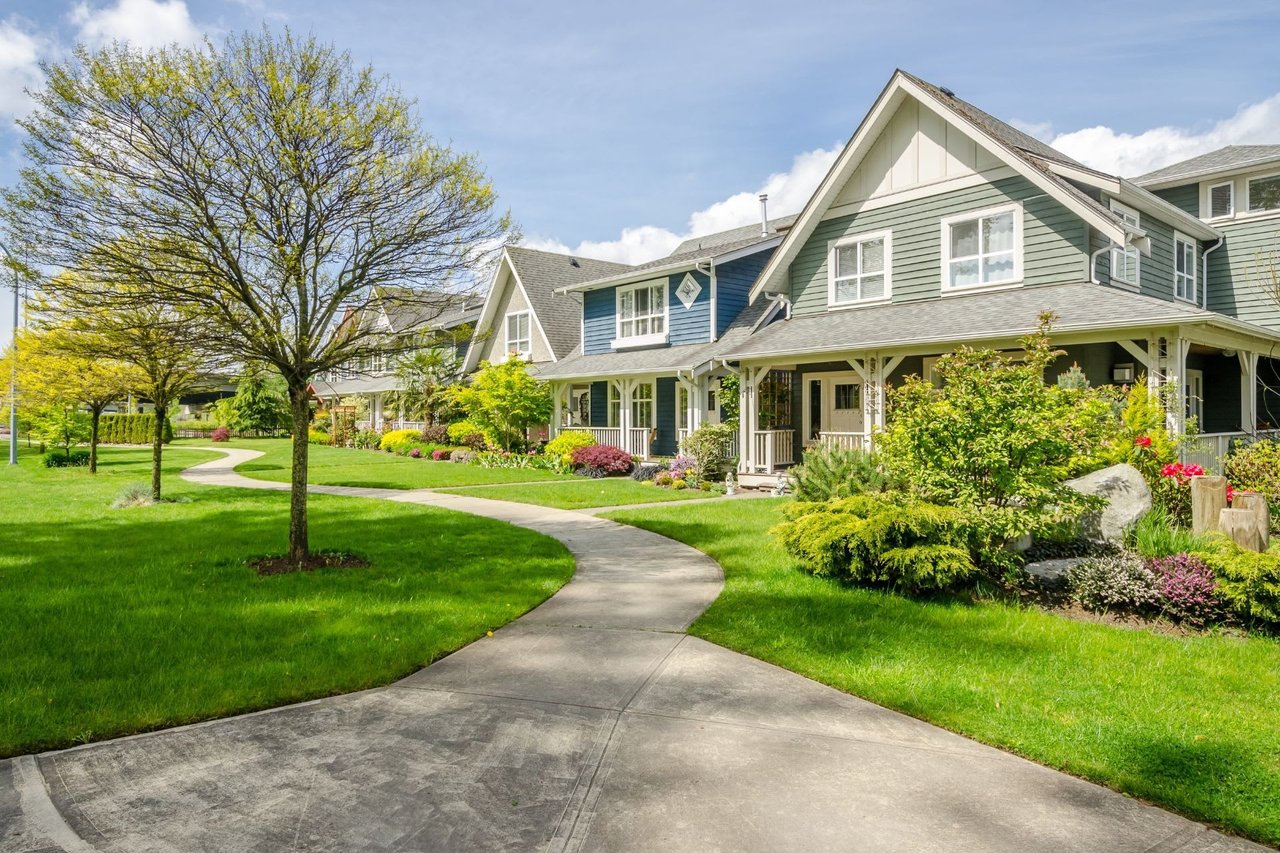 Luxury multi-family townhouse community showcasing a concrete walking trail, manicured common area greenspace, mature trees, and craftsman residential facades.