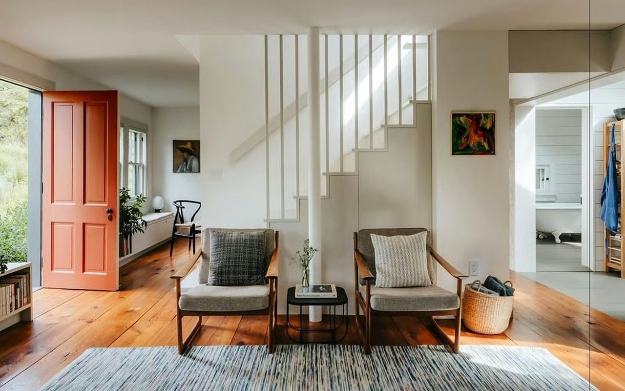 Furnished living area with two armchairs and an open red front door beside the staircase.