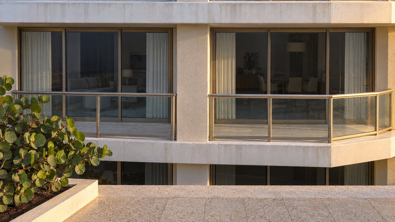 Two condominium balcony bays with glass railings, bronze-framed doors, and a leafy sea-grape plant.