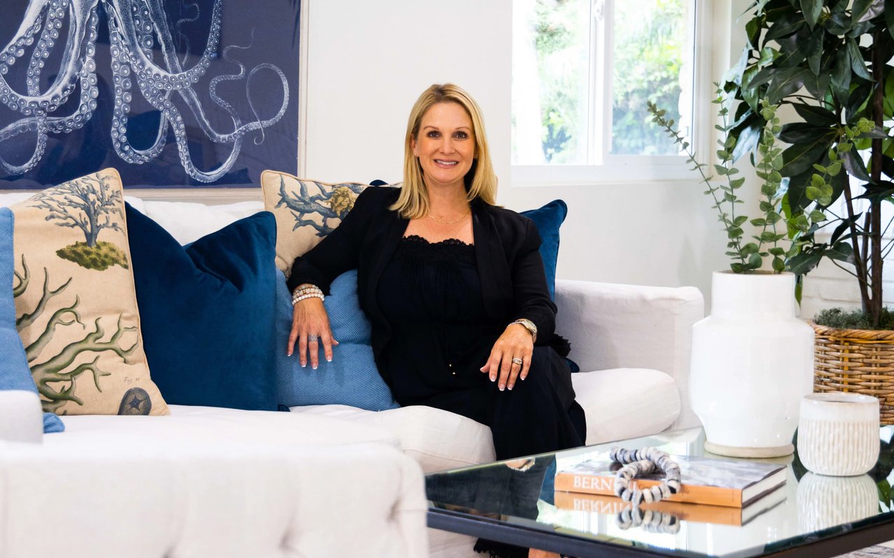 A woman is sitting on a white couch with blue and beige pillows in a living room.