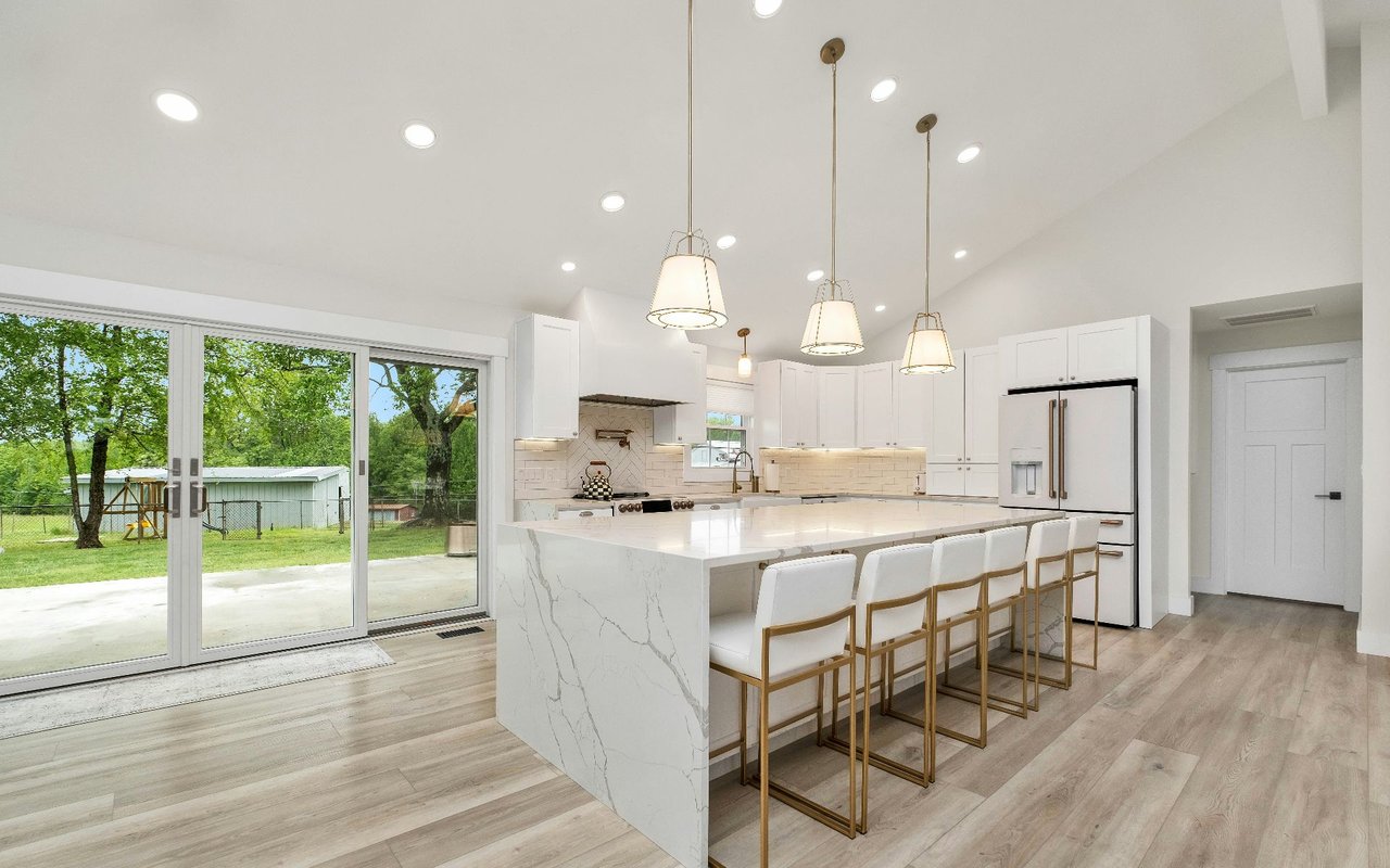 Modern white kitchen with a marble-look island, four stools, and sliding doors to the backyard.
