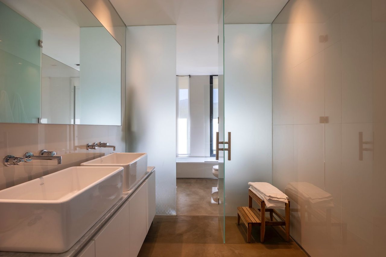 Modern bathroom with twin vessel sinks, a mirrored wall, glass partition, and towel bench.