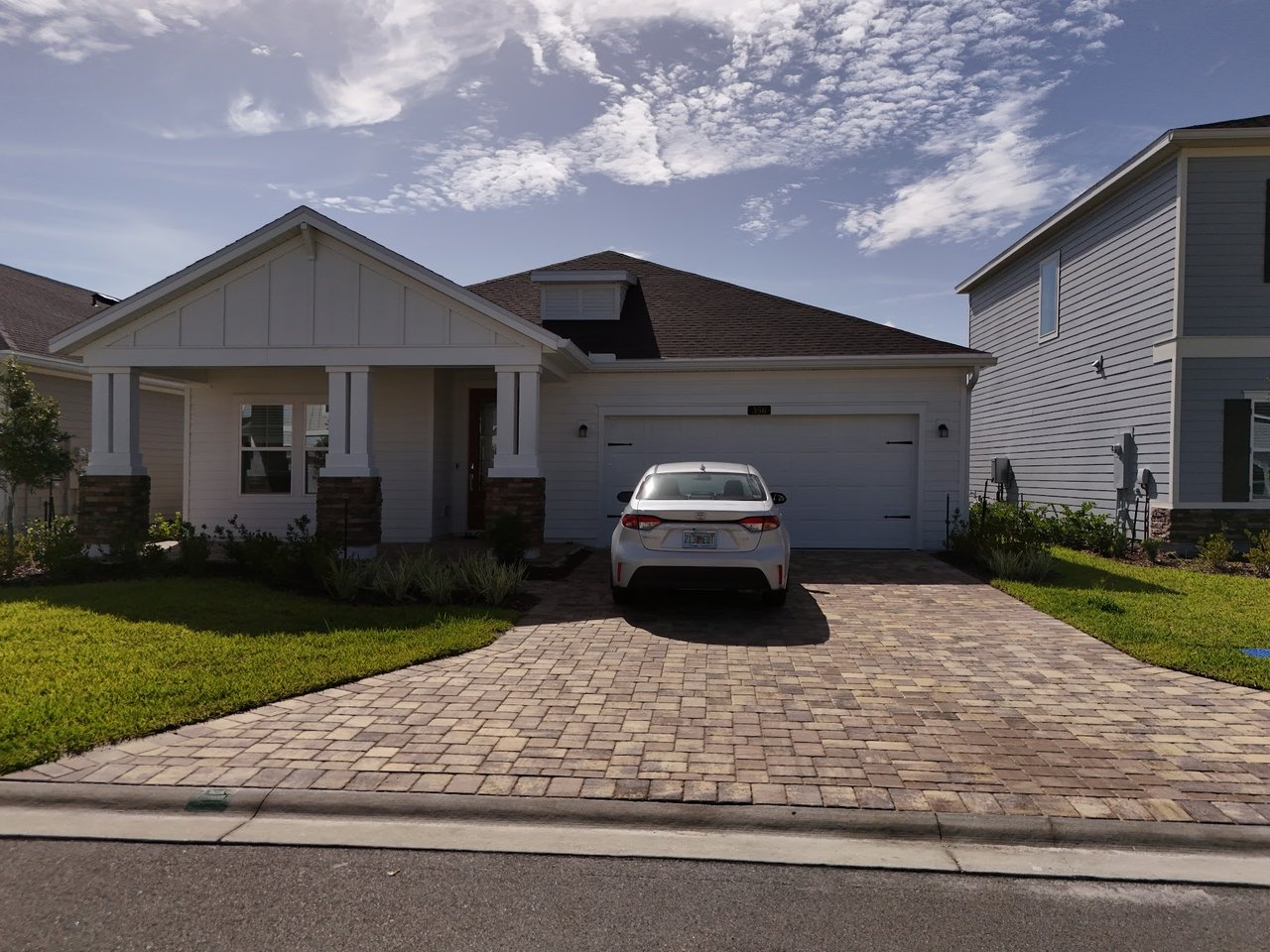 Single-story house with a covered porch, attached garage, and paver driveway with a white car.
