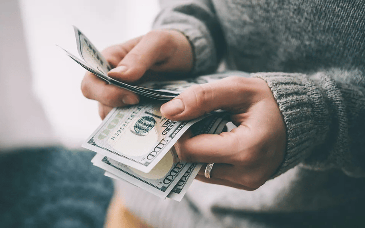 Hands count $100 bills, illustrating cash expenses.