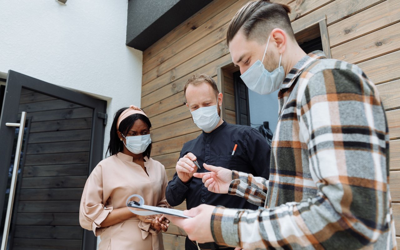 Masked adults review paperwork outside a modern wood-sided home.