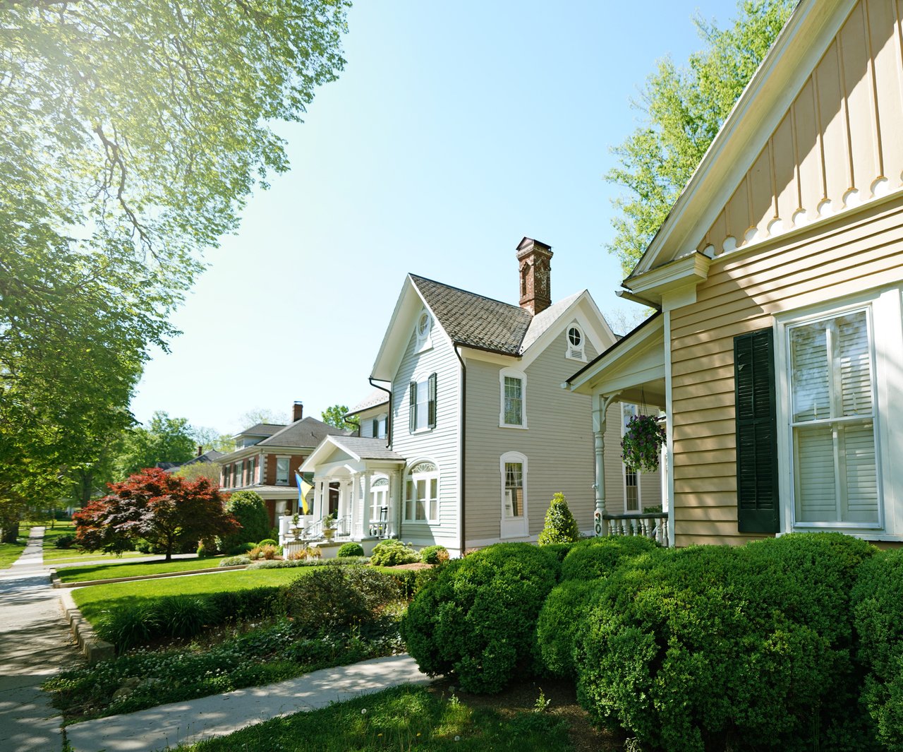Two-story Victorian-style house with a front porch, brick chimney, and leafy landscaping.