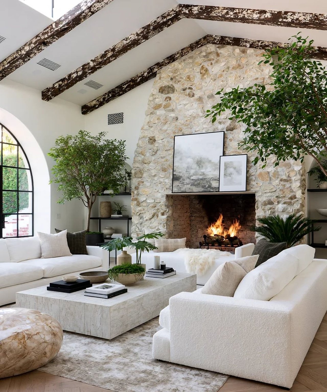 Living room with a stone fireplace, exposed beams, arched window, and white sofas.