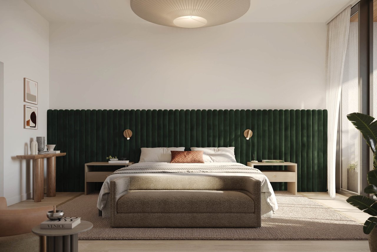 Staged bedroom with a dark green upholstered headboard, neutral bedding, and a sunlit window.