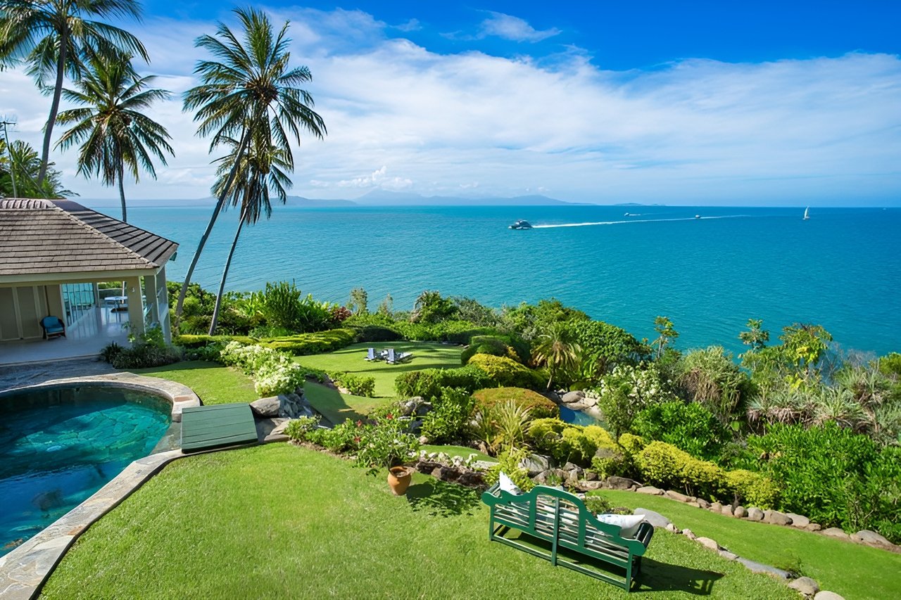 Oceanfront home with a pool and landscaped garden overlooking turquoise water and distant boats.