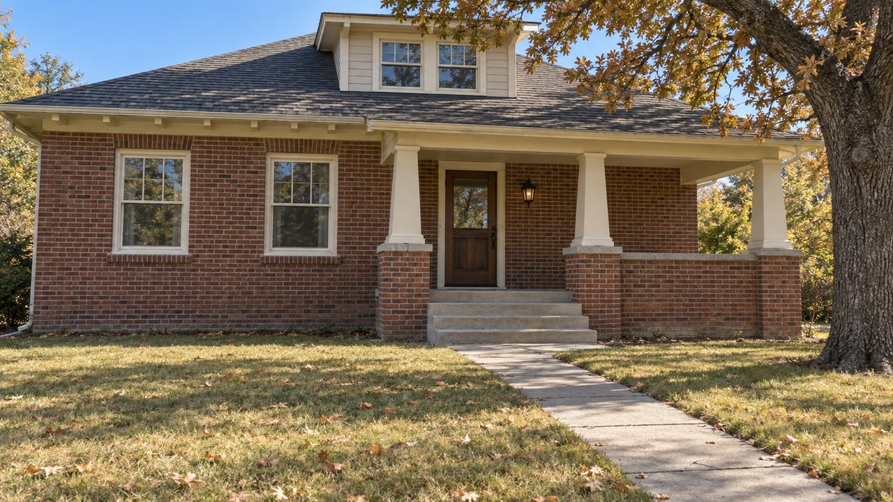 Brick home with cream porch trim, a deep autumn lawn and a mature oak in clear late-morning light.