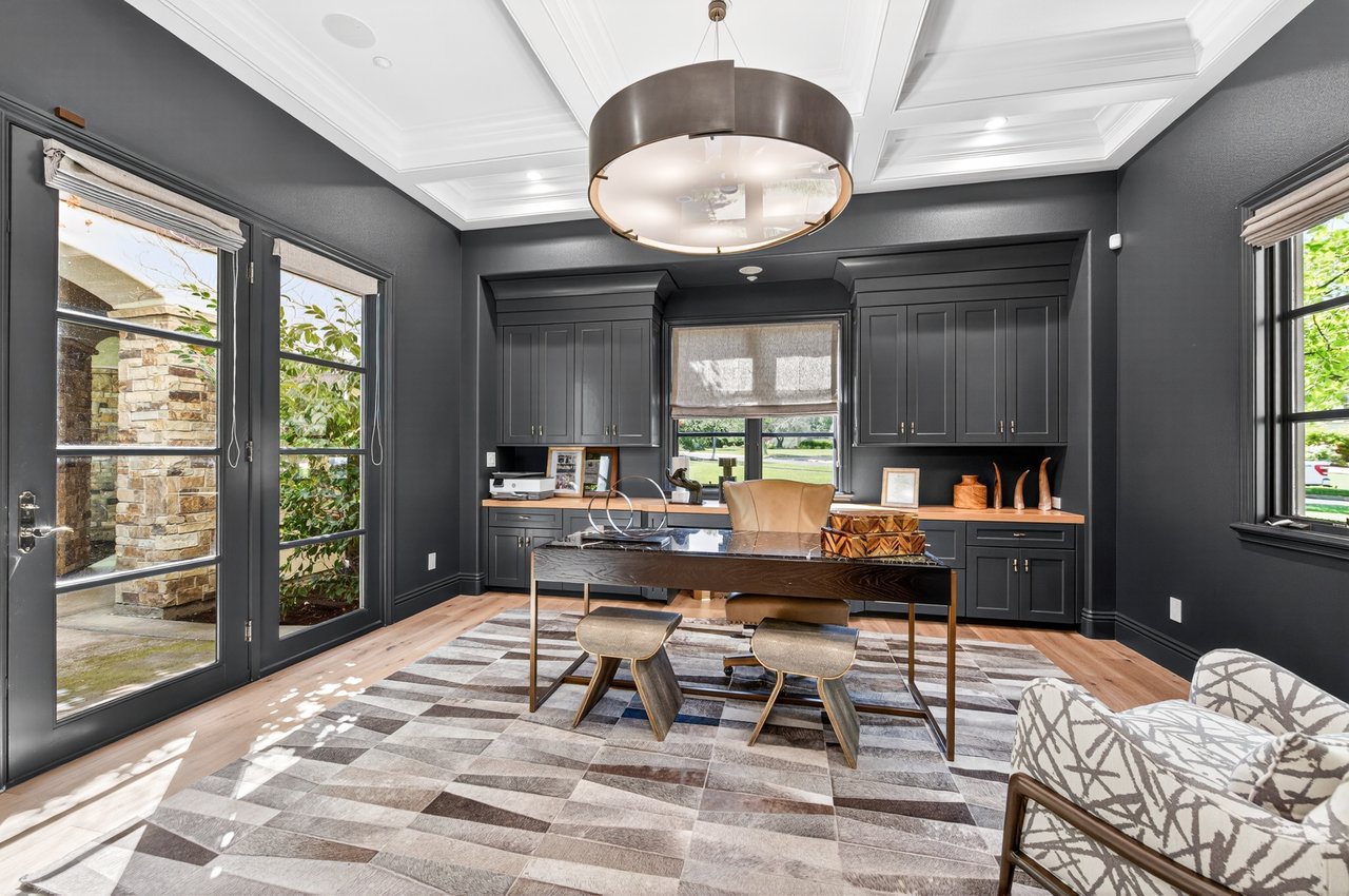 Home office with dark built-in cabinetry, a desk, patterned rug, and glass doors.