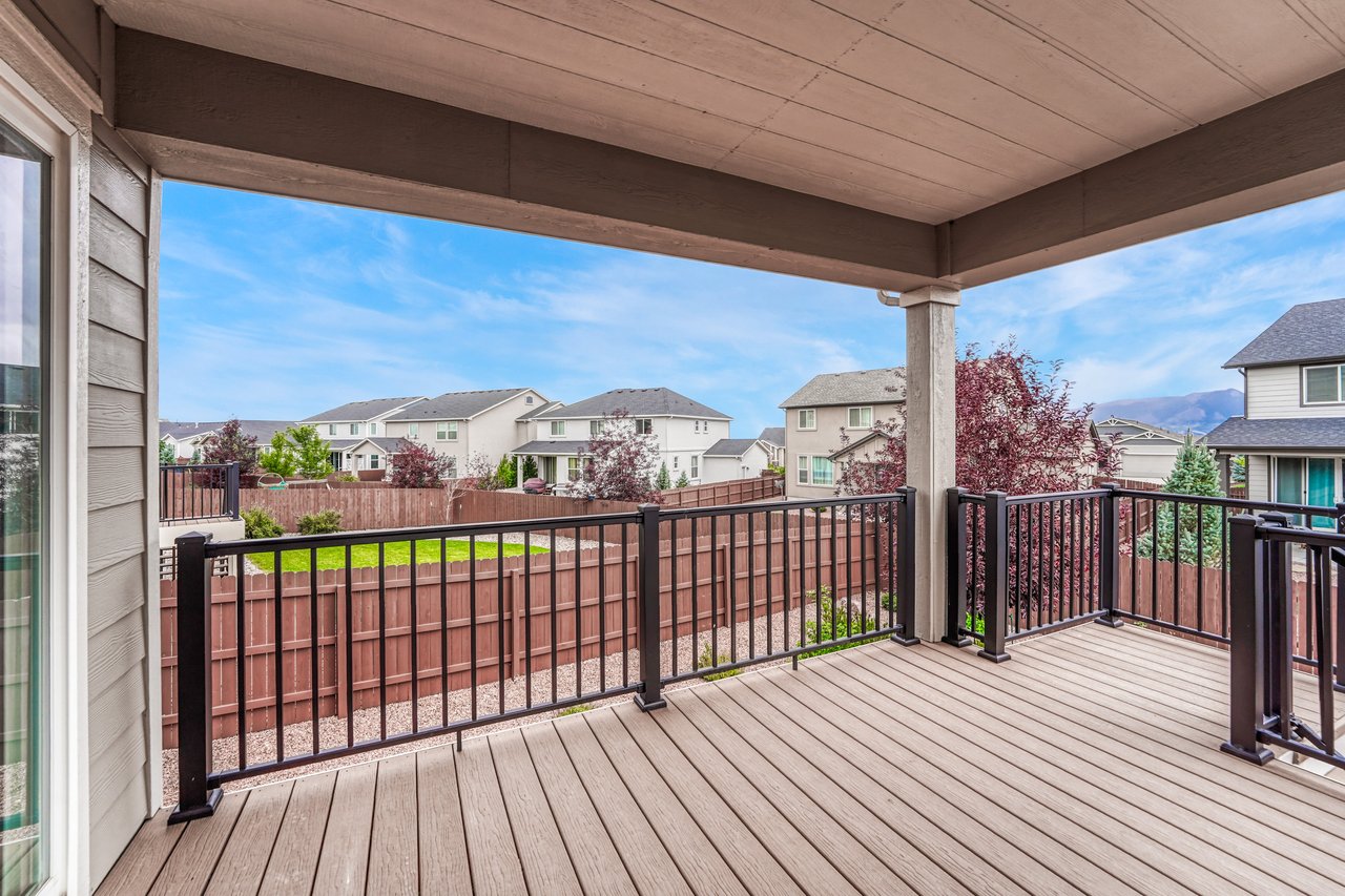 Covered back deck with metal railings overlooking the fenced back yard and mountain views