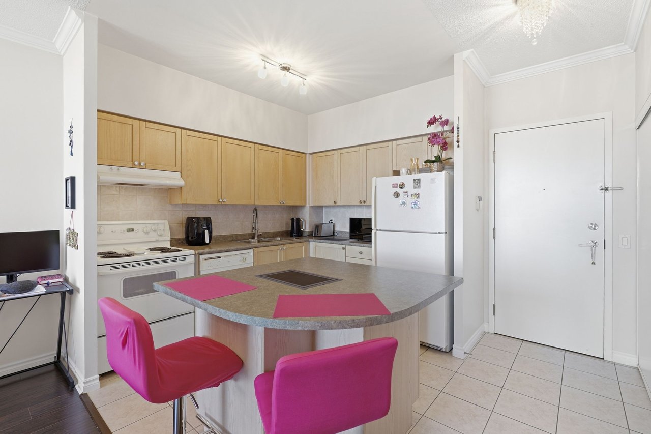 Condo kitchen with light wood cabinets, white appliances, and a breakfast island with bright pink chairs.