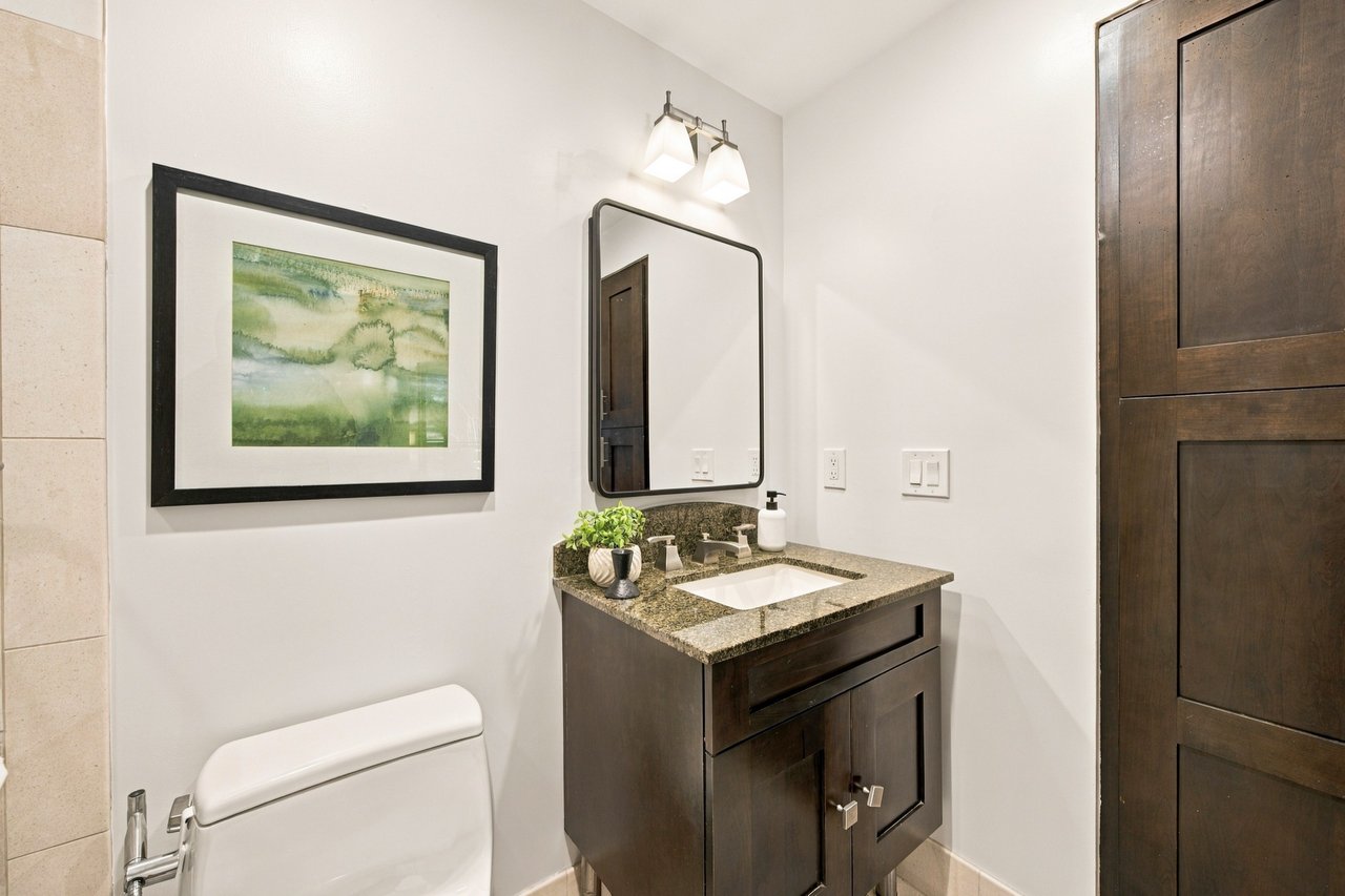 Bathroom vanity with a granite countertop, dark wood cabinetry, framed artwork, and a toilet.