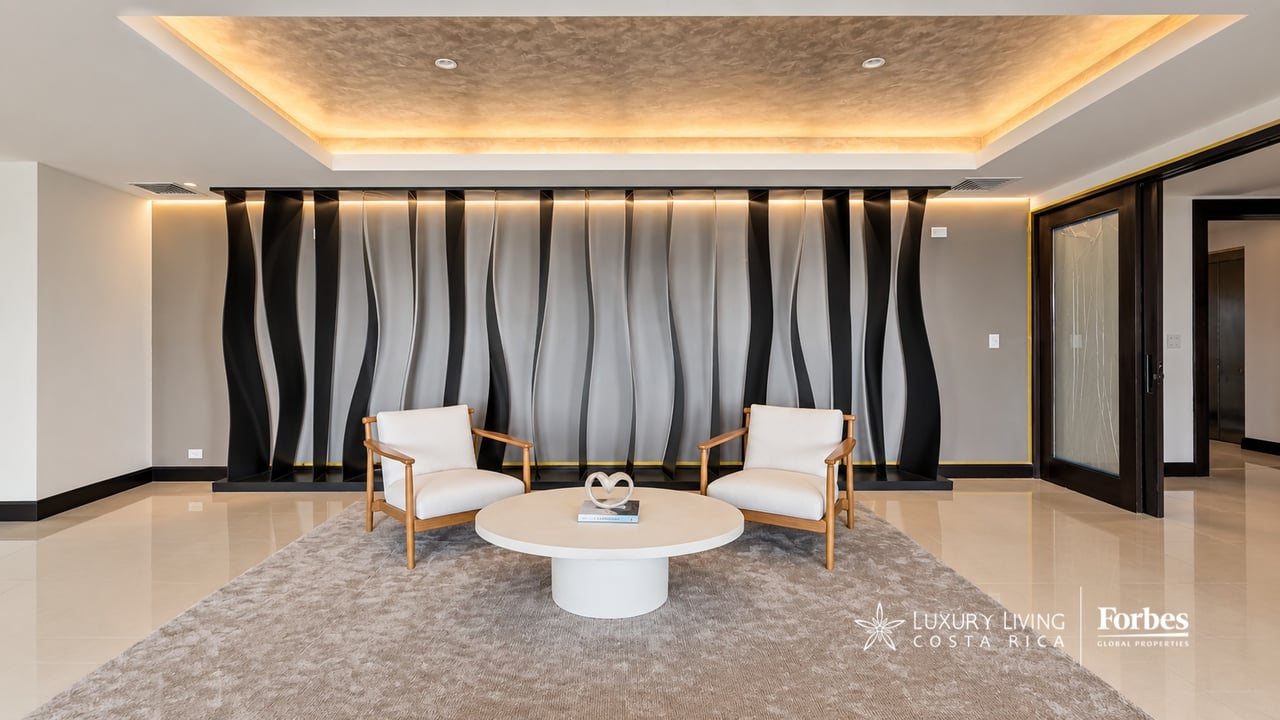 Penthouse seating area with two white armchairs, a sculptural black-and-white wall, and an illuminated ceiling.