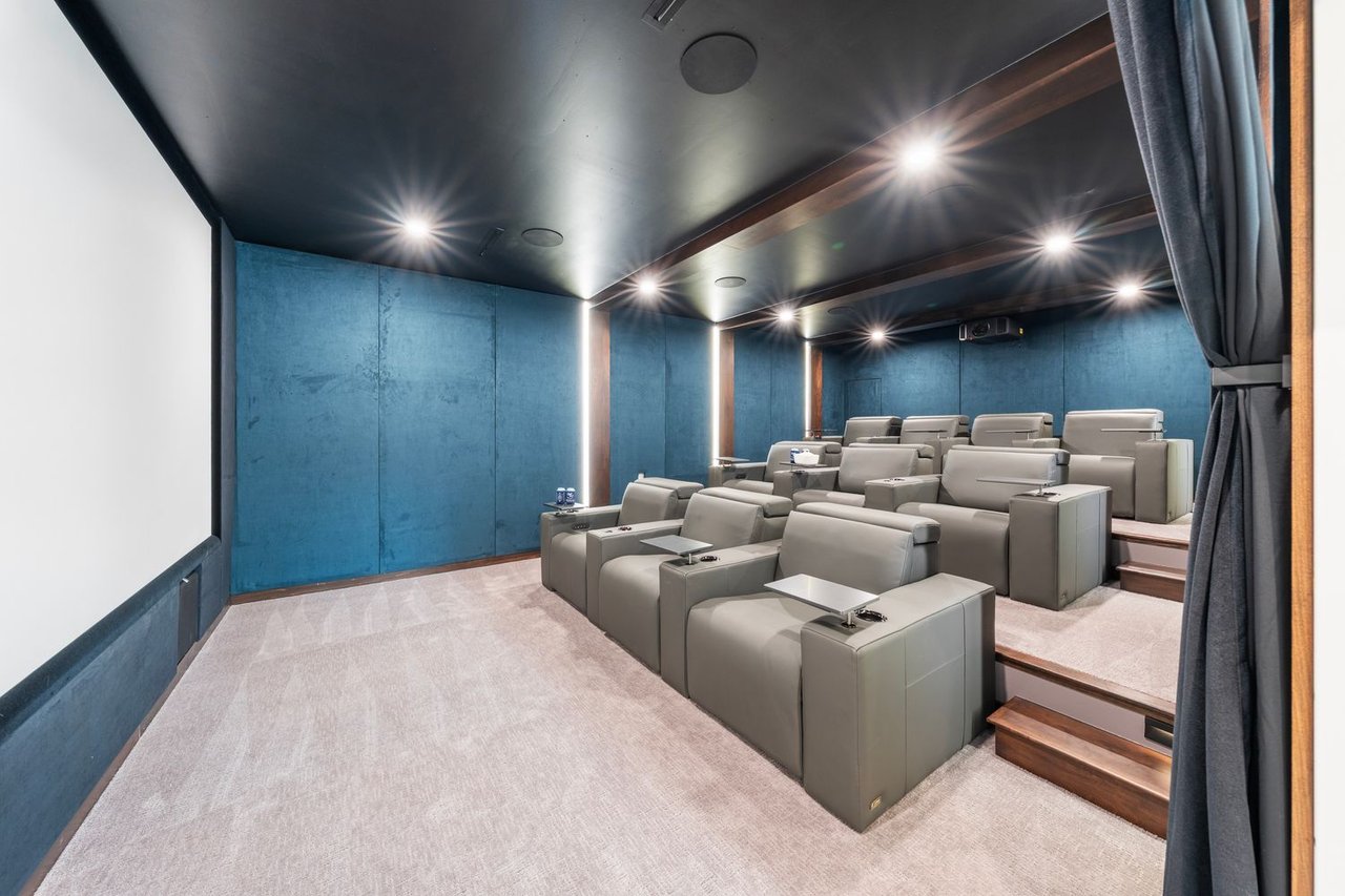 Home theater with rows of gray recliners, blue walls, and recessed ceiling lights.