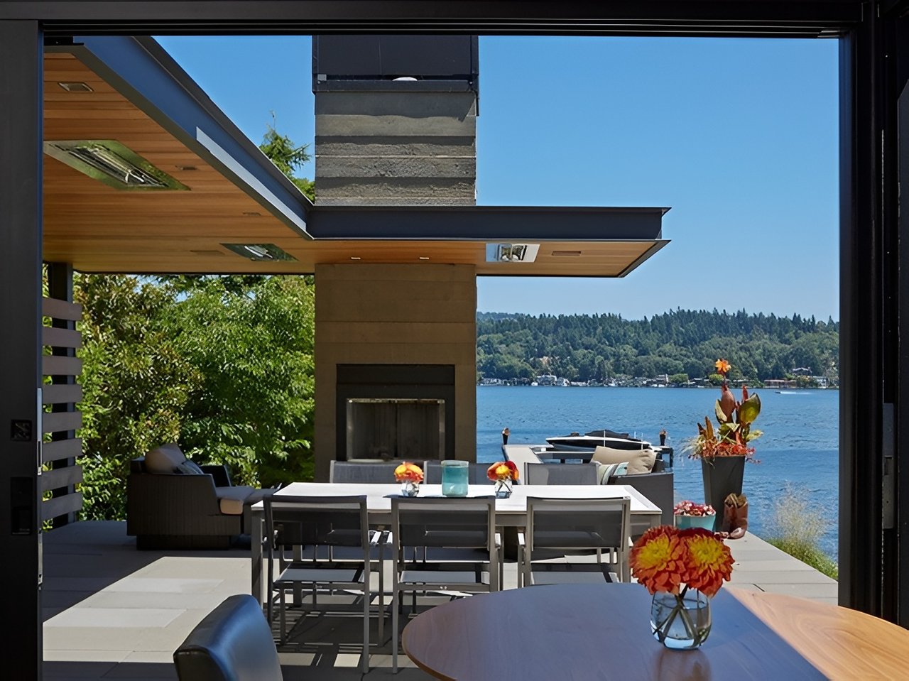 Lakeside patio with outdoor dining furniture and a view across the water to a wooded shore.